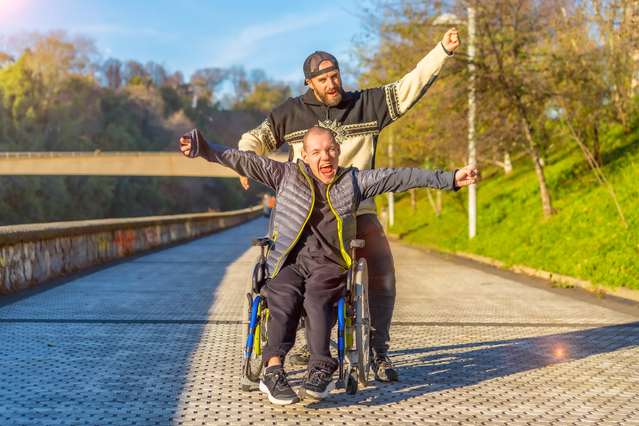 Disabled person in wheelchair with friend overjoyed, smiling, enjoying with arms up, vistoria, enjoying life in sunset of the city Zorgverlener houdt cliënt aan de arm